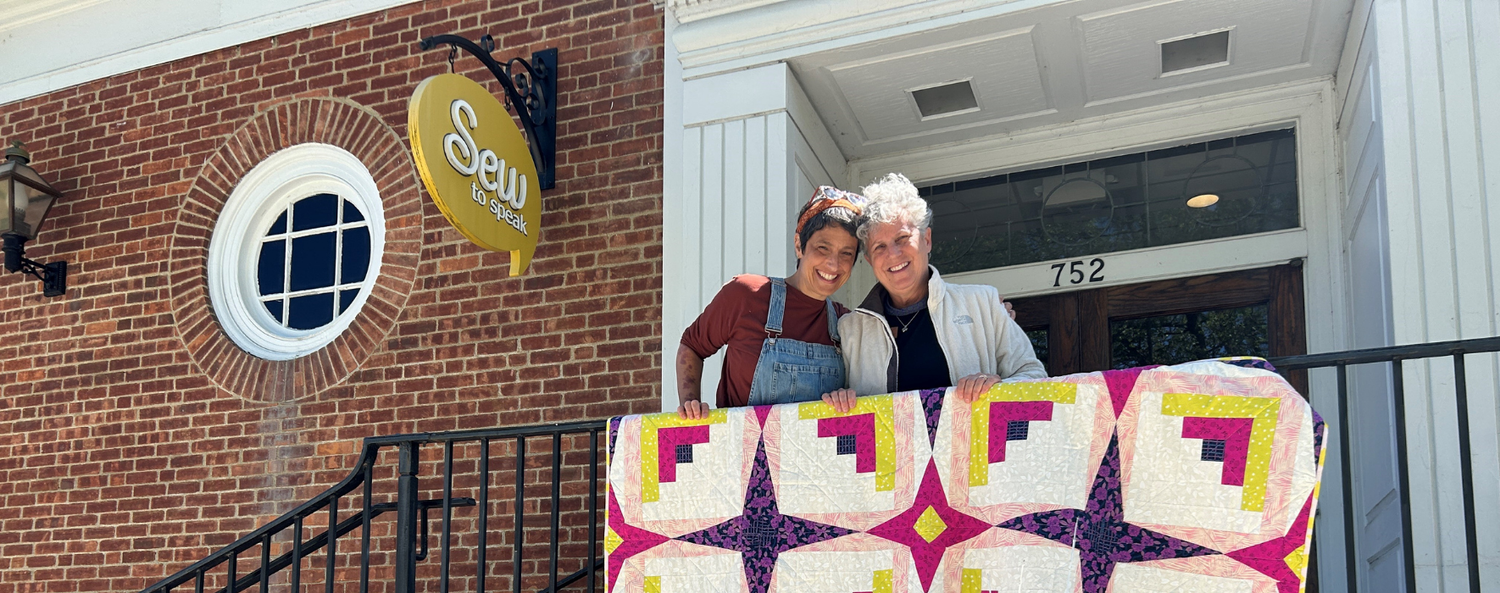 Eva Fried and Amy Baden, Owners of Sew to Speak Fabric Store in Columbus, OH. They're holding a quilt outside of the store.
