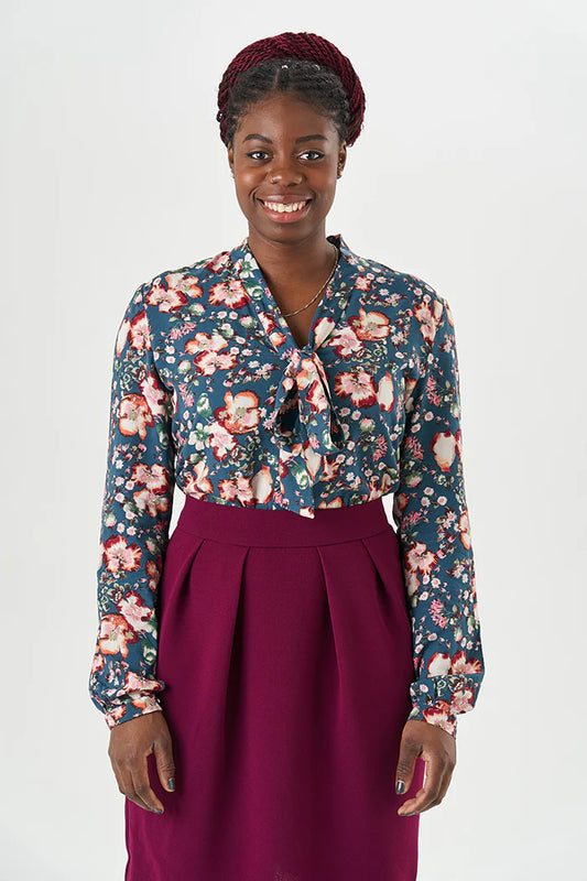 Woman wearing a hand sewn floral blouse and purple skirt on a white background.